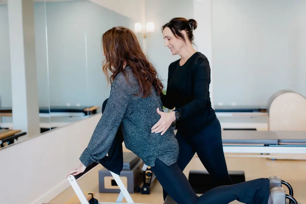 Pilates instructor guiding client on reformer machine in studio