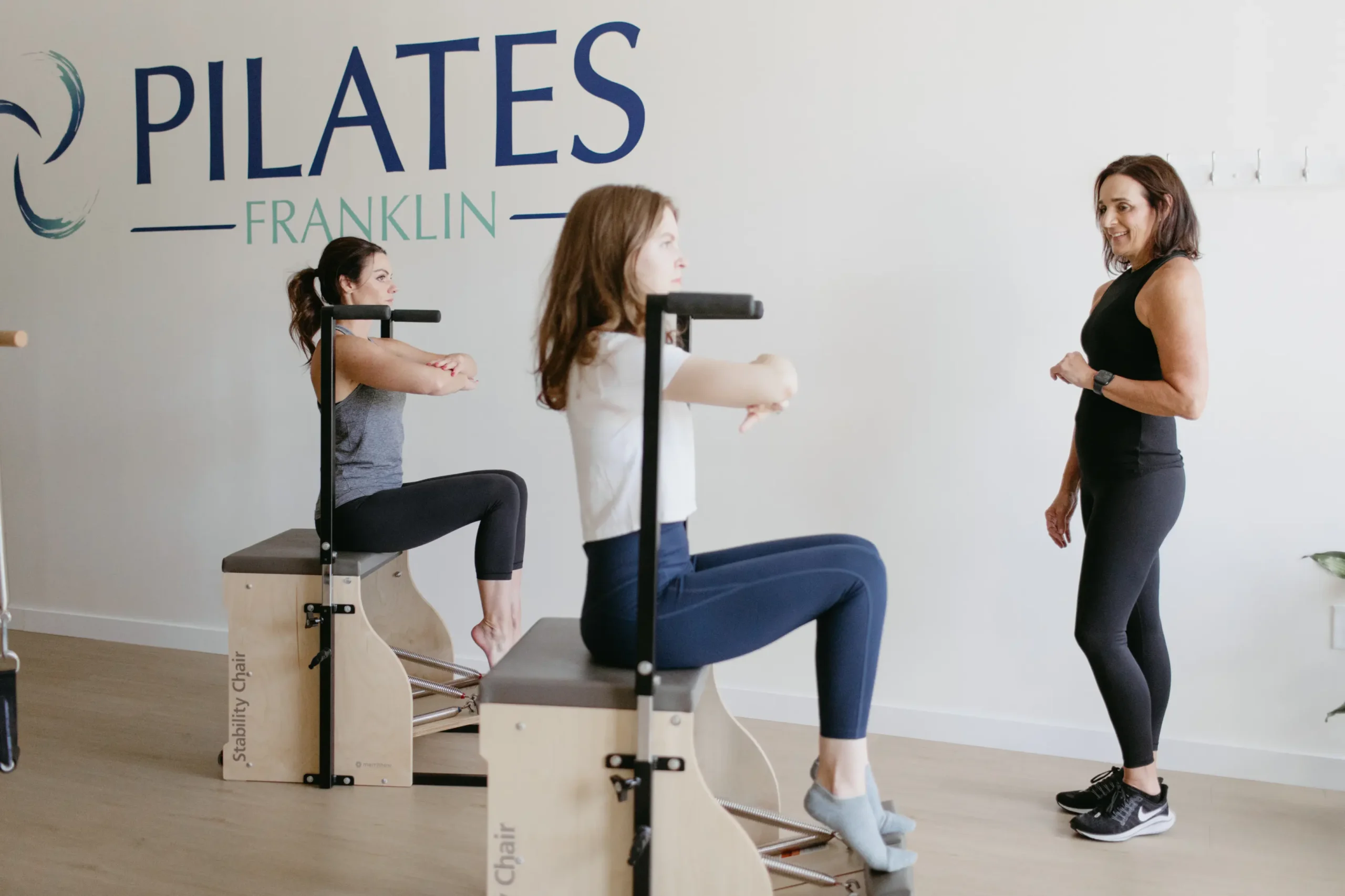 Pilates Franklin Instructor guiding two women on Pilates stability chairs at studio