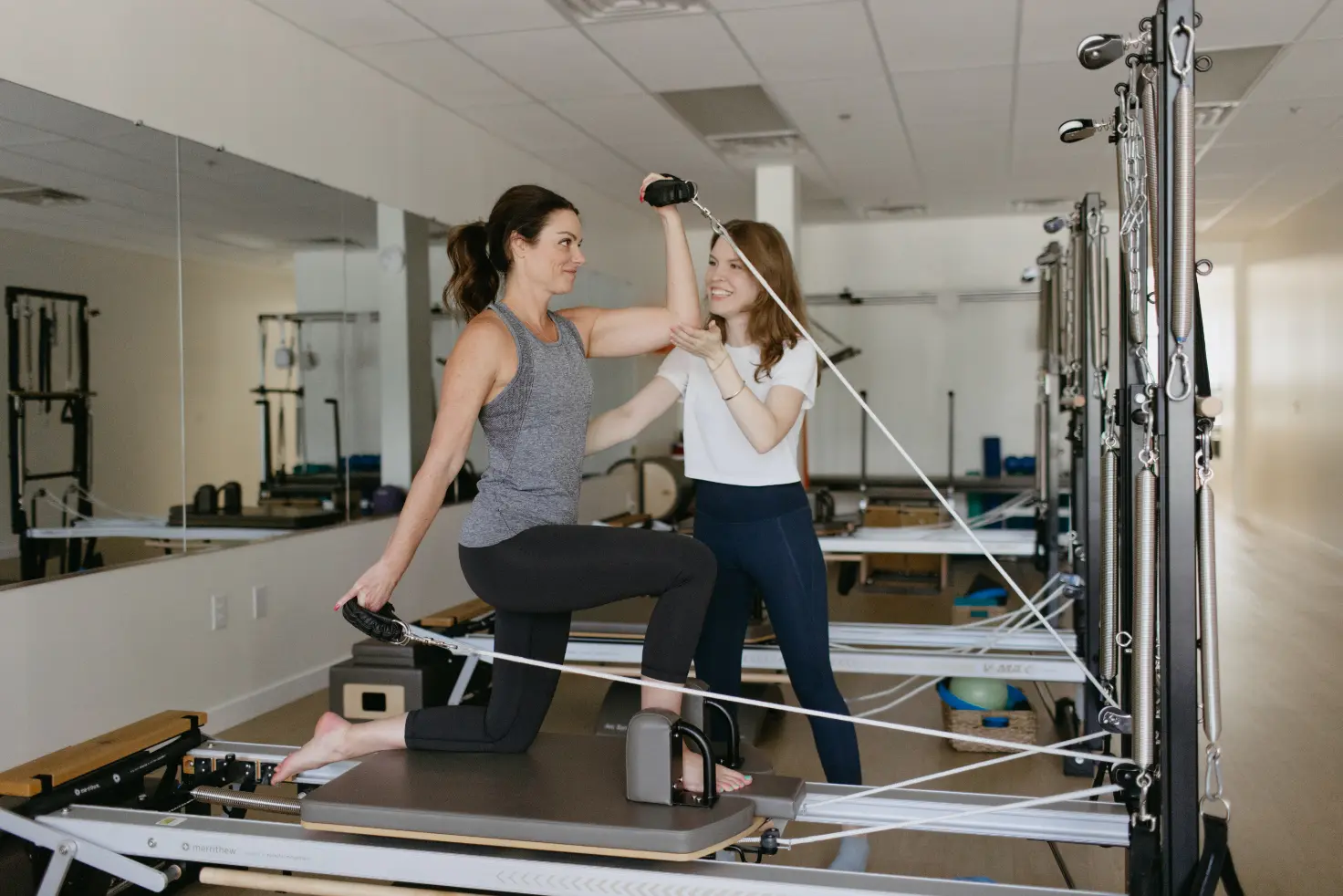 Pilates instructor guiding woman on reformer machine in studio