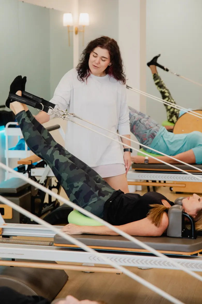 Pilates instructor guiding client on reformer machine in studio