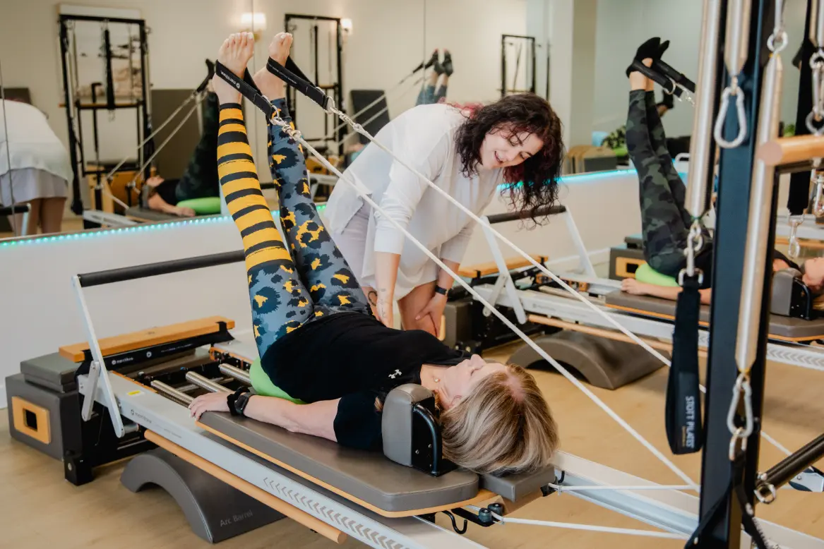 Pilates instructor guiding client on reformer machine in studio