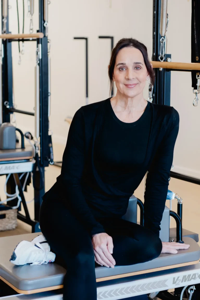Woman in black sitting on Pilates reformer machine smiling