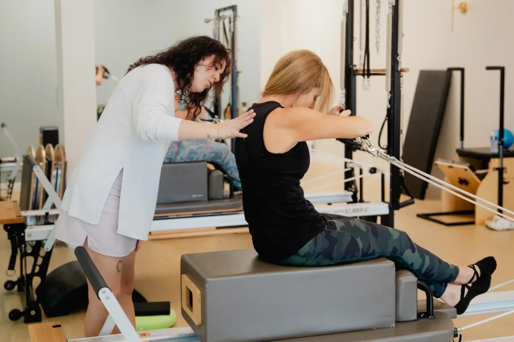 Pilates instructor guiding woman on reformer machine